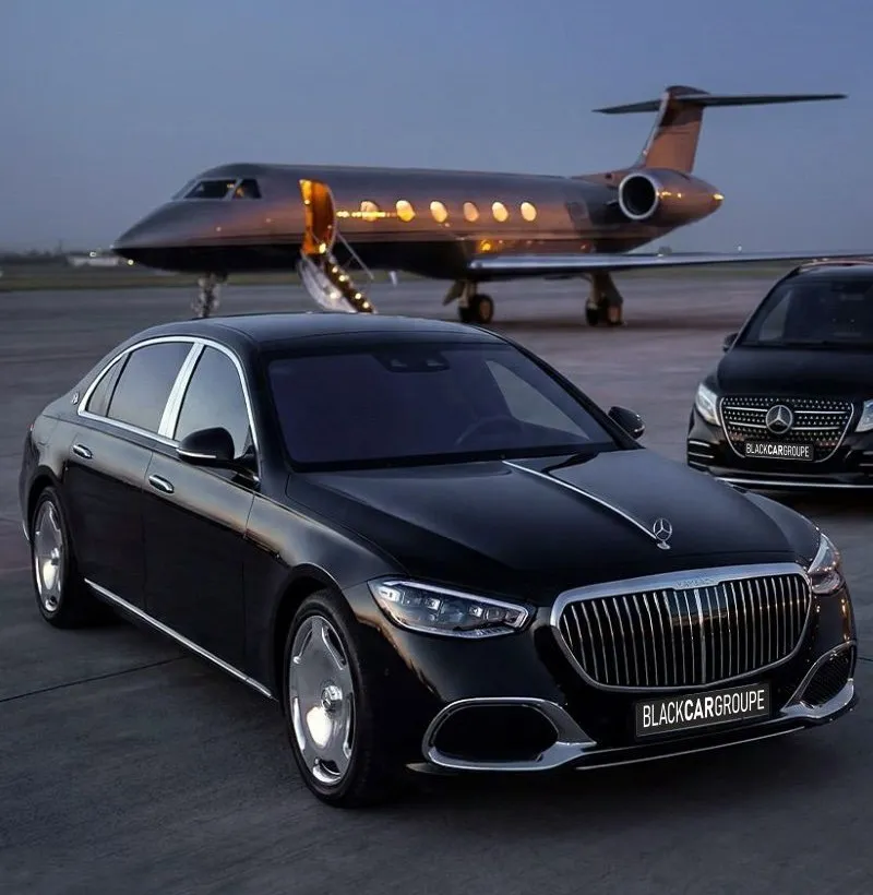 A black Mercedes-Benz S-Class and V-Class waiting beside a private jet on the tarmac at dusk