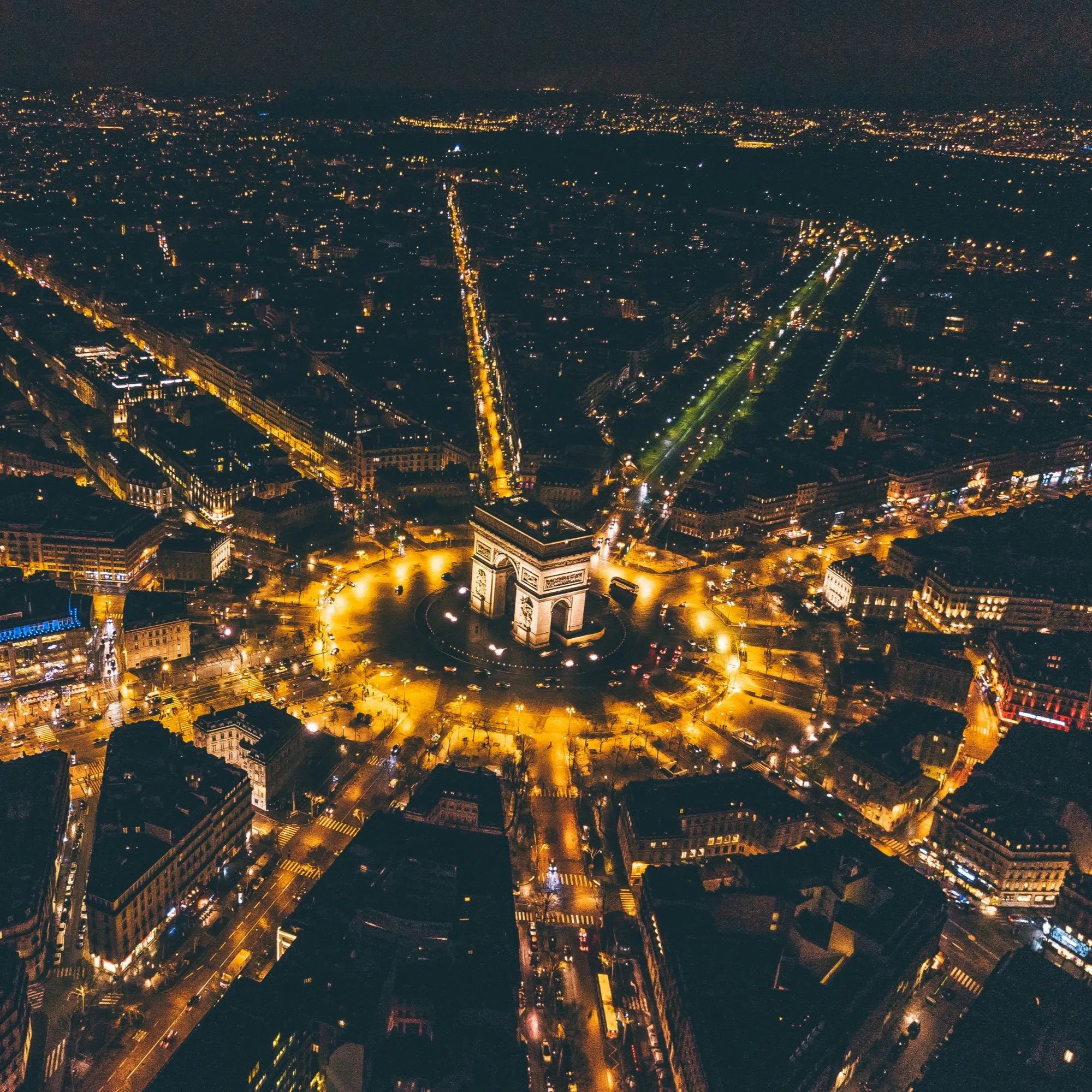 Paris at night from above, the avenues lit around the Arc de Triomphe